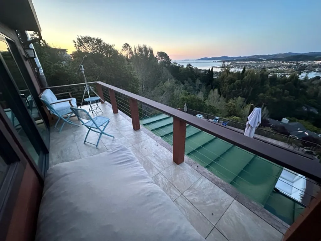 A tiled deck with chairs and a daybed cushion looking out over the bay at dusk