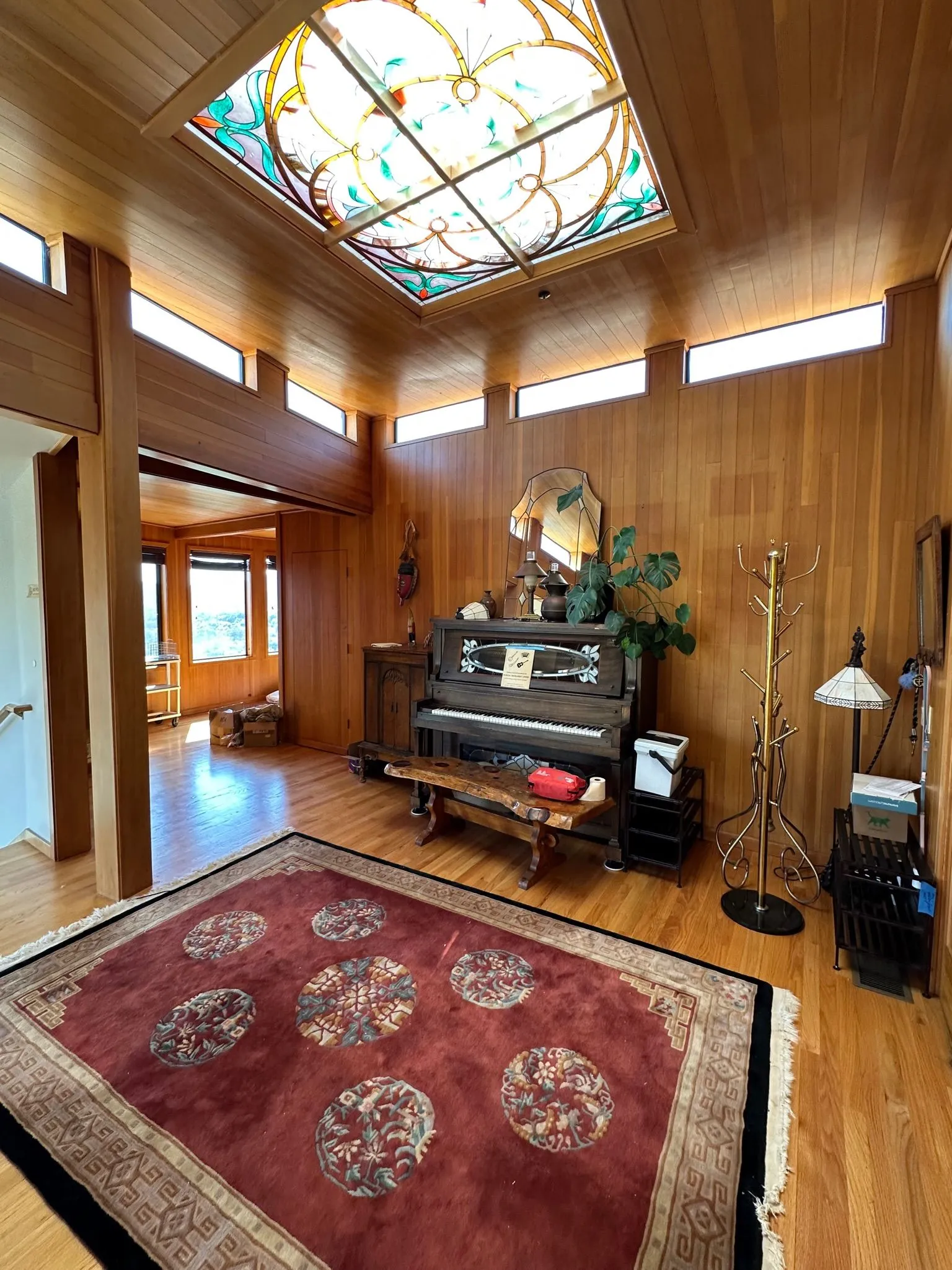 A wood-paneled foyer with an antique upright piano under an ornate stained-glass skylight