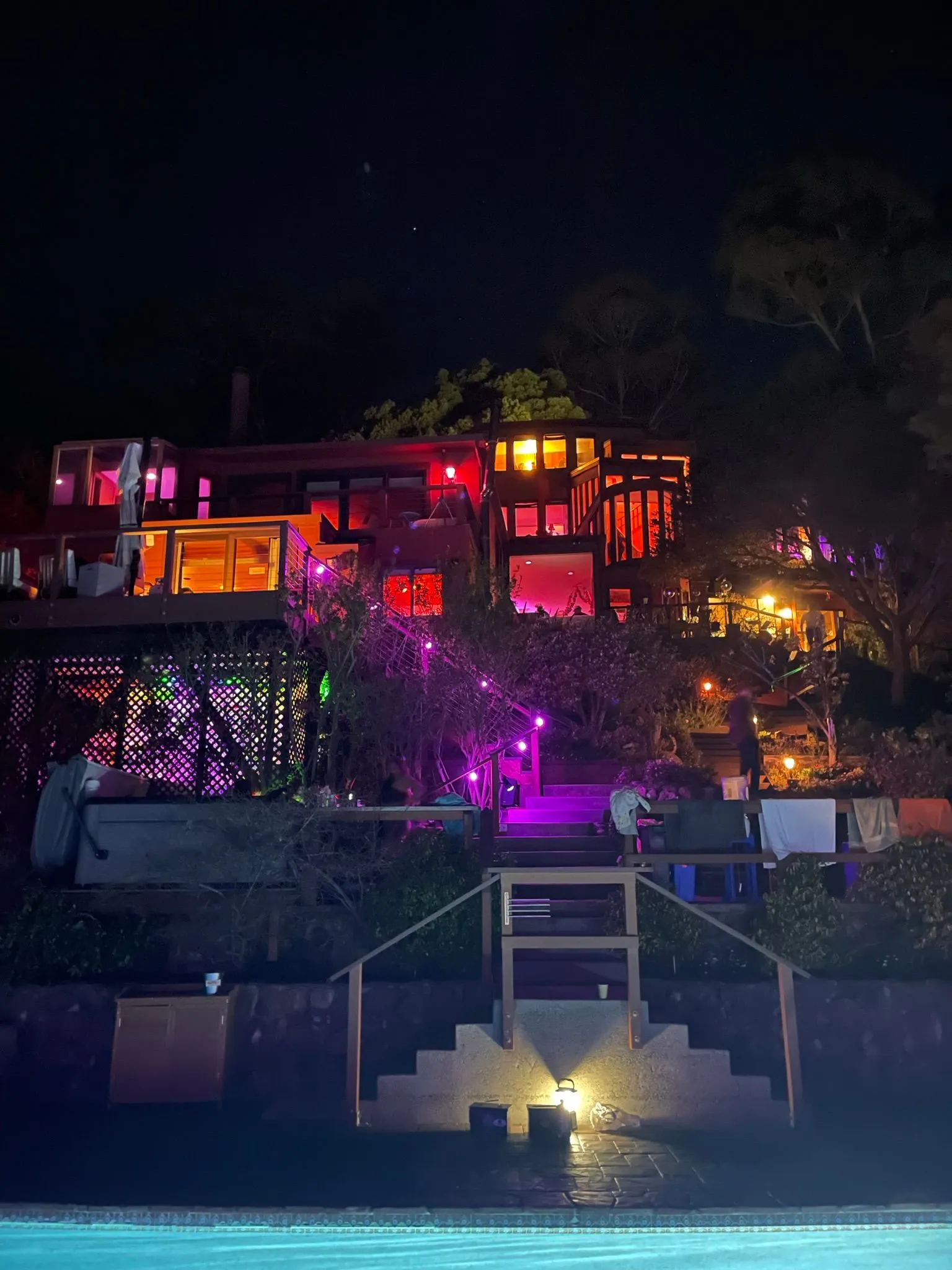 The house and pool at night, lit in shifting pink and amber programmable light