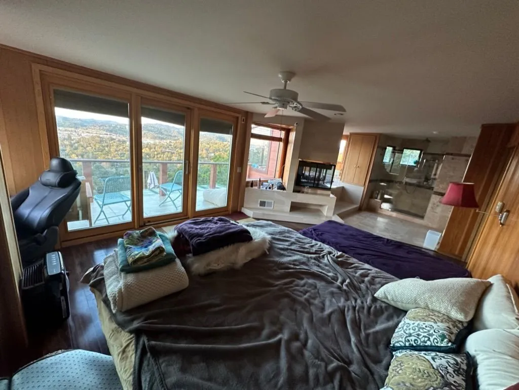A bedroom with large windows framing the surrounding hills and an en-suite spa area