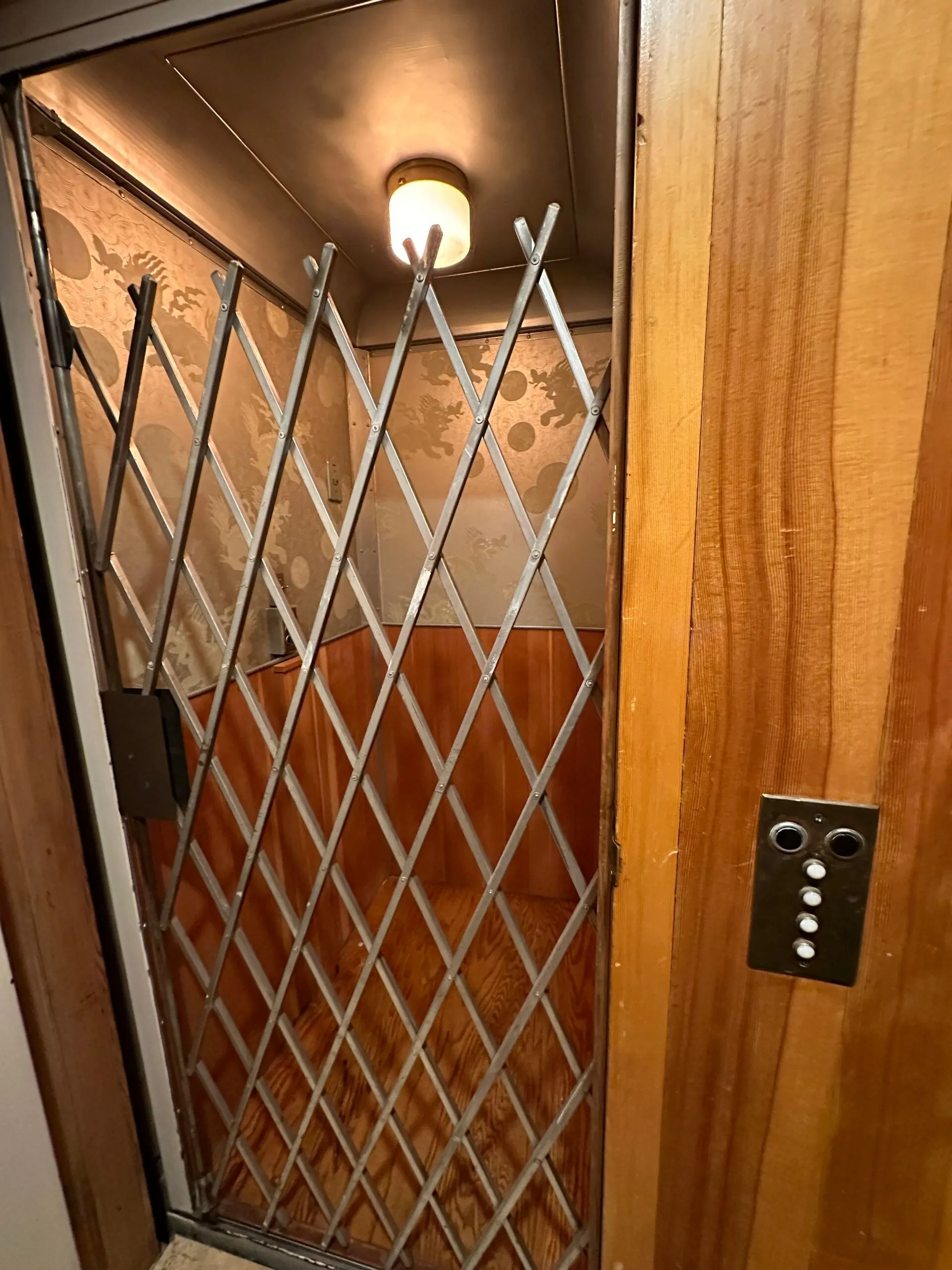 The restored 1953 elevator with its folding metal gate and dragon-patterned walls