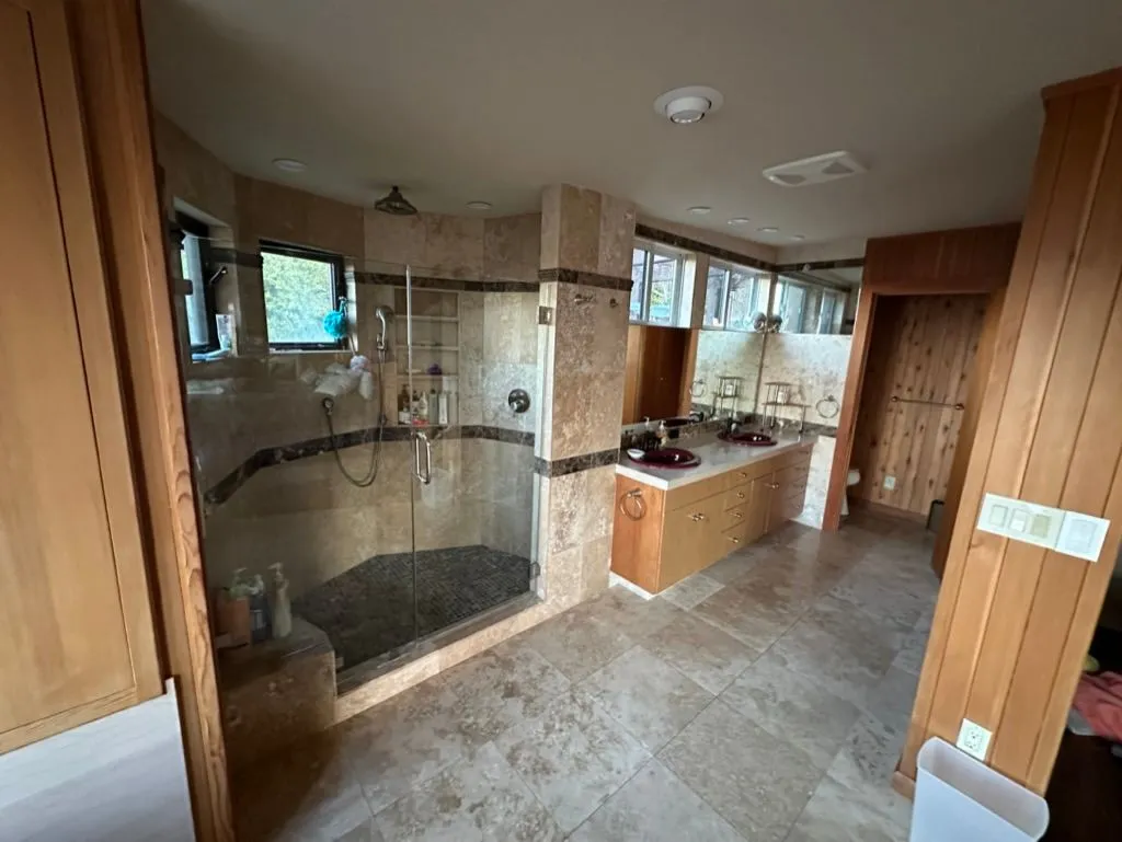 A large travertine bathroom with a glass walk-in shower and a double vanity